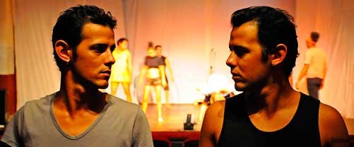Dos jóvenes en primer plano, segundo plano tabloncillo de teatro