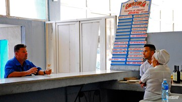 Hombre con billete en primer plano, dependienta conversando